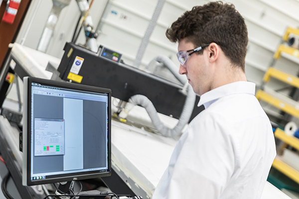 Employee working at a computer wearing a lab coat and goggles