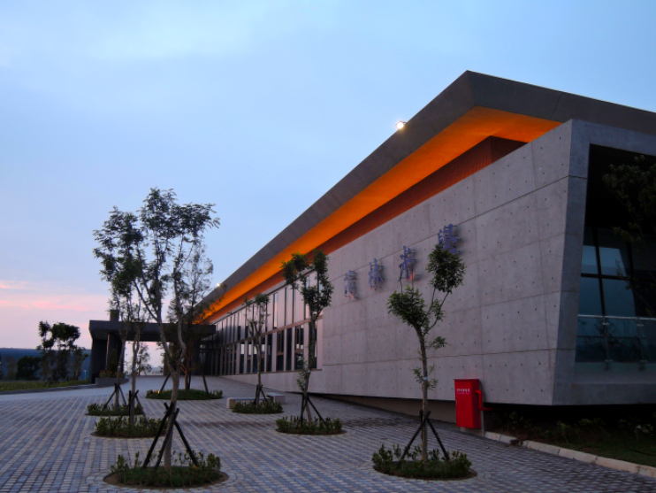A sunset view of our Tongluo, Taiwan facility that shows a brick courtyard, trees, and the up lit roof of the facility.